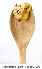 A Close Up Of A Blob Of Raw Chocolate Chip Cookie Dough On The End Of A Wooden Spoon Against A Bright White Background.