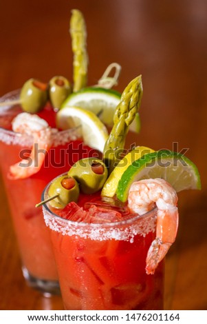 close up of a bloddy mary cocktail served on a wooden bar top garnished with a salted rim veggies and a shrimp