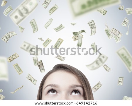 Close up of a blond teen girl s head near a gray wall dollars falling around her. Concept of suddenly becoming rich