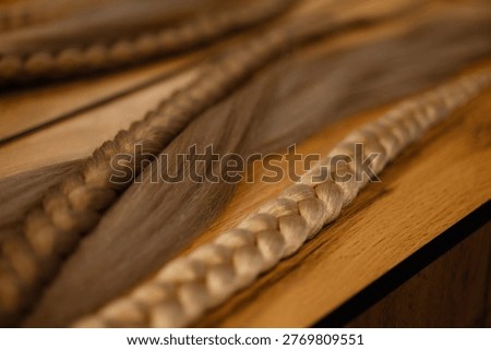 Close up of blonde braid extensions with metal rings on wooden table, front view. Concept hair extensions, beauty products, natural tones, hairstyling materials, salon workspace.