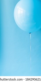 Close up of a blue balloon on a string against a blue backdrop.
