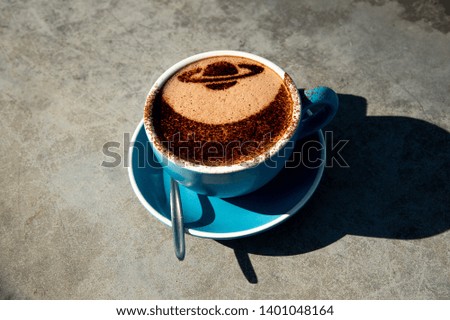Close up blue cup of hot chocolate with cocoa powder Saturn shape decoration and shadow on cement table blur background at Mount John Observatory , South island New Zealand.