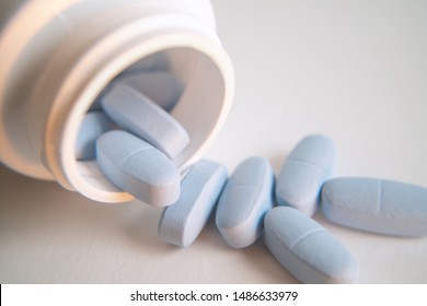 Close up of blue pharmacology tablets spilling out of pill white medicine bottle isolated on white.