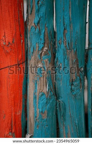 close up of blue and red painted wooden fence  poles tied together paint peeling wire embedded into wood paint layer weathered and peeling off to reveal natural wood fence post under paint vertic