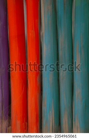 close up of blue and red painted wooden fence  poles tied together paint peeling wire embedded into wood paint layer weathered and peeling off to reveal natural wood fence post under paint vertic
