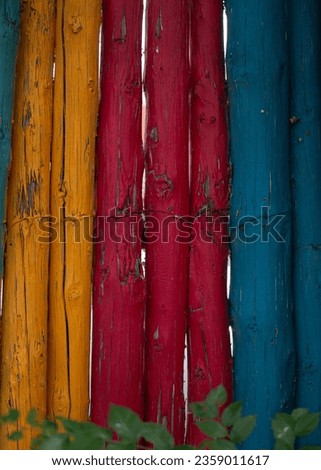 close up of blue red yellow painted wooden fence poles tied together paint peeling wire embedded into wood paint layer weathered and peeling off to reveal natural wood fence post under paint vertical