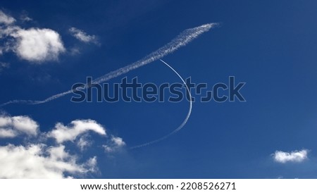Close up of blue sky with white clouds in sunshine with vapor trails of a er whose pilot is enjoying his flight while making a turn