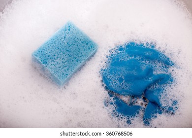 Close Up Of Blue Sponge And Rag In Kitchen Sink Full Of Foam