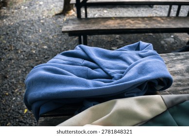 close up of a blue sweater and a backpack placed on a rustic wooden bench in an outdoor cafe garden with gravel ground portraying a relaxing leisure break atmosphere