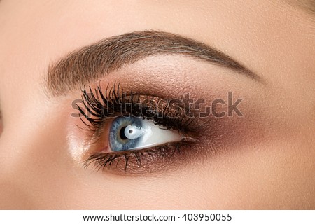 Close up of blue woman eye with beautiful brown with red and orange shades smokey eyes makeup. Modern fashion make up.