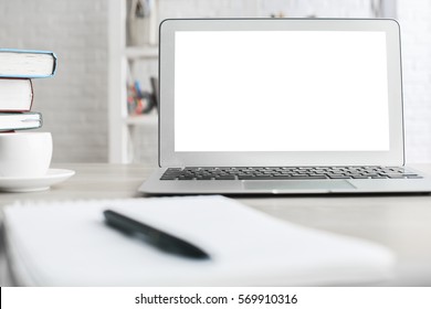 Close Up Of Blurry Notepad With Pen, Blank White Laptop Screen, Coffee Cup And Books On Office Desktop. Mock Up