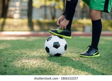 Close up boot of football player which puts his leg on ball and tying shoelace on soccer stadium on the training. - Powered by Shutterstock