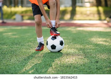 Close Up Boot Of Football Player Which Puts His Leg On Ball And Tying Shoelace On Soccer Stadium On The Training.