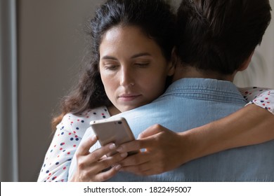 Close Up Of Bored Young Caucasian Woman Hug Man Texting Messaging With Lover On Smartphone Online. Unhappy Wife Embrace Husband Cheating On Web On Cellphone. Family, Relationship Problem Concept.