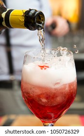 Close Up Of A Bottle Of Prosecco While The Barman Is Pouring It Into A Red Cocktail