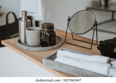 Close Up Of Bottle With Soap Dispenser, Mirror, Bath Salt, Clean And Fresh Rolled Towels In Bathroom. Wooden Shelf On Empty And Contemporary Tub. Selective Focus. House Decor At Bright Home