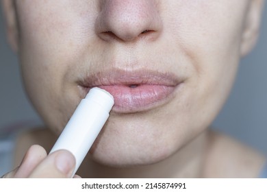 close up of bottom of the face of a woman using natural ingredients lip balm, white blank pack. Putting Lip Protector Lipstick on, hygienic balm from wax with honey add. lips home care.