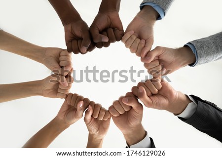Close up bottom view diverse employees team holding fists in circle, expressing unity and power in teamwork, multiethnic business people engaged in team building activity at briefing