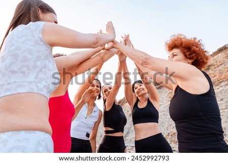 Close up bottom view of group of Caucasian fit women in sportswear high five. Wild beach in background. Concept of girl power and sports competition.