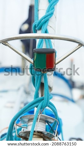 Close up of the bow of a sail boat in a marina, with lines, ropes and navigational lights in focus.