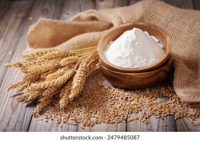 Close up of bowl of flour, wheat grains and spikelets on wooden table
