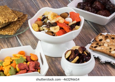 Close Up Of Bowl With Trail Mix, Goldfish Crackers, Granola Bars And Almond Biscuits - Delicious Snacks On A Wooden Background.