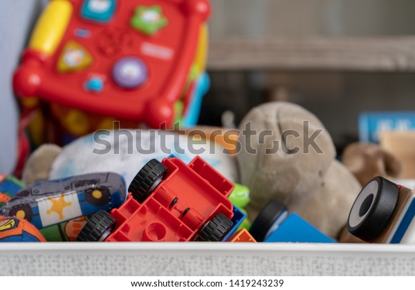 Close up of a box of\
toys, with many different objects including soft toys, play cars\
and toddler toys.