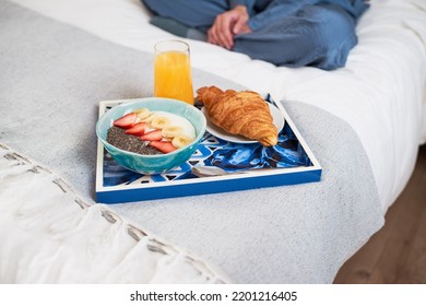 Close Up Of Breakfast Tray With Croissant, Fruit Bowl On Bed With Woman Sitting