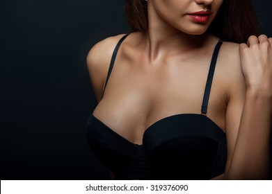 Close up of breast of attractive woman presenting her black bra. She is touching her shoulder gently. Isolated on black background and there is copy space in left side