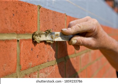 Close Up Of A Brick Wall And Jointer Trowel Used By The Worker To Apply And Level The Mortar Between Bricks