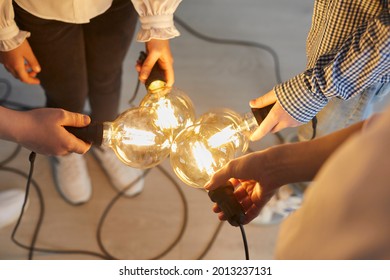 Close up of bright light bulb in the hands of children and teachers that mean a new idea. Teacher and her younger students connect light bulbs together as a symbol of collective thinking and teamwork. - Shutterstock ID 2013237131