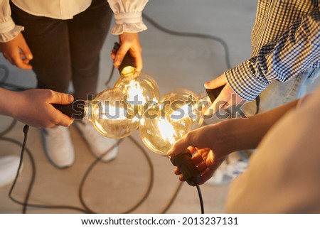 Close up of bright light bulb in the hands of children and teachers that mean a new idea. Teacher and her younger students connect light bulbs together as a symbol of collective thinking and teamwork.