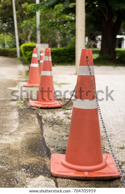 Close up bright orange traffic cones standing in a\
row on asphalt. concrete sidewalk with yellow red and white traffic\
sign. Road construction works. Traffic cones at tropical\
street