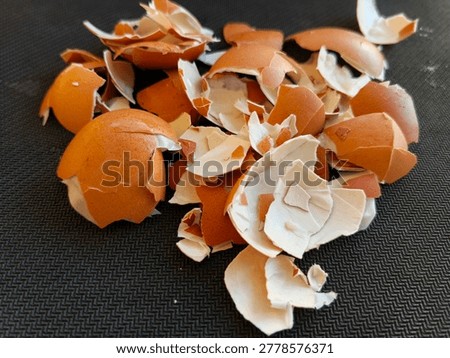 Close up of broken brown eggshell fragments scattered on dark textured surface. Natural organic food waste concept with rustic aesthetic and macro photography style.