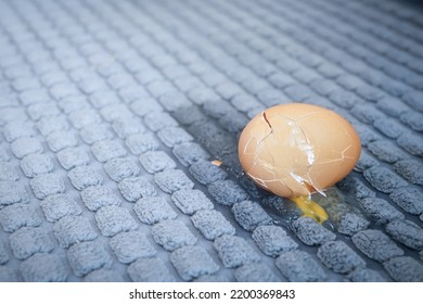 Close Up Of A Broken Egg On The Grey Rug In The Modern Kitchen. A Cracked Egg On The Carpet. Dirty Floor Mat Carpet. Copy Space For Your Text. Selective Focus.