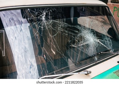 
Close up of a broken windshield of an old car. The glass pane has two impacts and cracks. Maybe after a riot, accident or demonstration in the city
