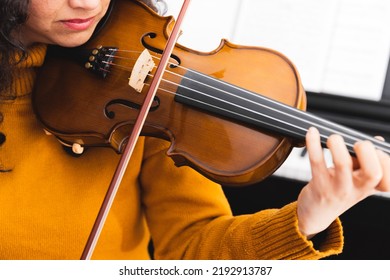 Close Up Brunette Concert Woman Wearing A Yellow Sweater, And Playing Violin By Reading Sheet Music.