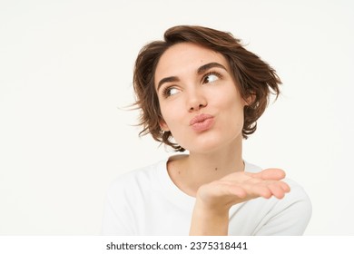 Close up of brunette woman blowing air kiss, mwah, kissing gesture, pucker lips and gazing away, standing over white background. Copy space - Powered by Shutterstock