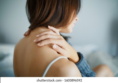 Close up of a brunette woman massing her neck in a bedroom