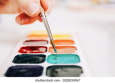 Close up brush is mixing colors of paints on palette. Watercolor paints and paint brush. Concept of art education, art class or studio and art therapy. Water color palette of paints.