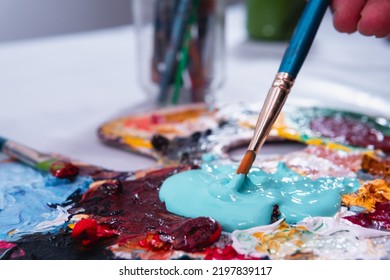 Cerca de un pincel que toma pintura acrílica de una paleta llena de muchos puntos de color.