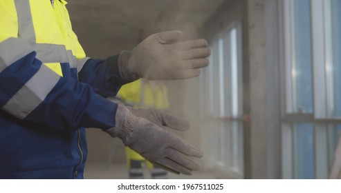 Close Up Of Builder Shaking Off Dust From Gloves At Construction Site. Cropped Shot Of Construction Worker Dusting Off Protective Gloves Doing House Renovation