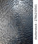 Close up of a bumpy and wrinkled black textured surface with glossy finish. Abstract dark industrial background or metallic pattern backdrop.