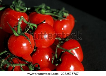 close up of bunch of fresh cherry tomatoes with green stems isolated on dark grey background