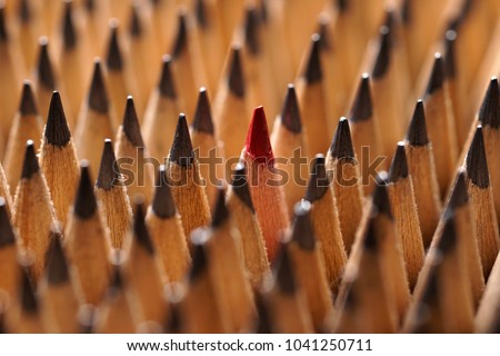 Close up of bunch of identical sharp black graphite pencils and one different, unique red pencil that stands out. Shallow depth of field. Studio shot. Concept of diversity. Concept of uniqueness.