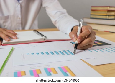 Close up Business man using pen pointing on notebook looking stock market chart and Presentation on the tablet. in office. 