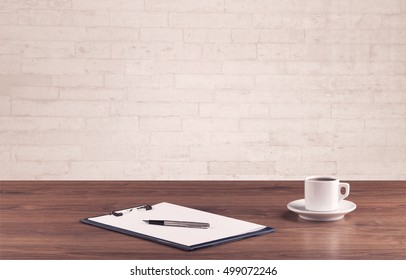 Close Up Of Business Office Desk With Pen Board Coffee In Front Of Empty White Brick Textured Wall Background.