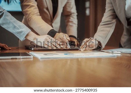 Close up of business team hands using pens to review charts on paper at a conference table, collaborative meeting and planning concept