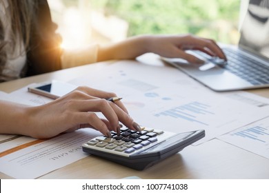 Close up Business woman using calculator and laptop for do math finance on wooden desk in office and business working background, tax, accounting, statistics and analytic research concept - Shutterstock ID 1007741038