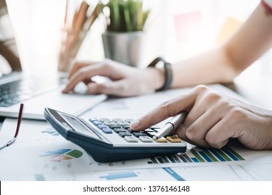 Close up Business woman using calculator and laptop for do math finance on wooden desk in office and business working background, tax, accounting, statistics and analytic research concept - Shutterstock ID 1376146148